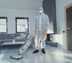 A person in protective coveralls vacuuming a contemporary living room.