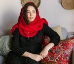 A woman in a red scarf and black dress sits indoors, showcasing traditional style.